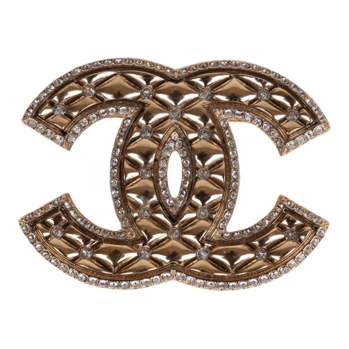This brooch is in?gold tone metal with clear crystals on?a quilted CC logo.