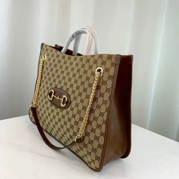 this spacious tote features a large double-handled silhouette and a chain shoulder strap for a touch of contemporary flair. Its organizational interior and magnetic snap closure add functionality to its stylish design.The Gucci 1955 Horsebit Large Tote Bag pays homage to the original bag that inspired the line over six decades ago