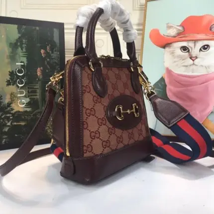 a stunning addition to the Horsebit 1955 line. This mini top handle bag is expertly crafted from Gucci’s iconic monogram canvas in a beige and ebony colorway. The contrasting dark brown leather details add a touch of sophistication to the design.Drawing inspiration from the original Gucci bag that inspired this line over six decades ago